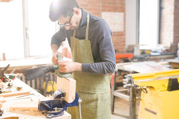 Portrait of focused modern carpenter sanding wood in joinery shop standing at table  in sunlight, copy space