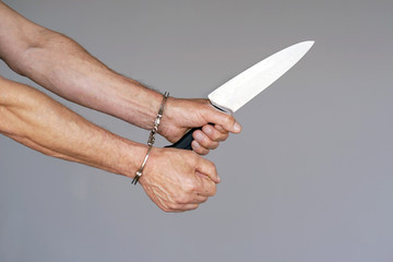 Close-up. Arrested man holding a knife. Handcuffed hands isolated on gray background. Prisoner or...