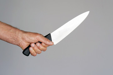 Hand of a man holding a knife isolated on a gray background . Big kitchen knife in man hand.