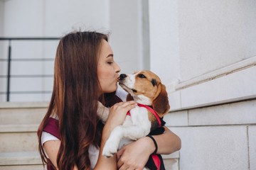 Beautiful young brunette woman kissing cute little beagle puppy outdoors
