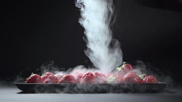 A stream of liquid smoke is poured onto a plate of strawberries. Berries lie on a plate.