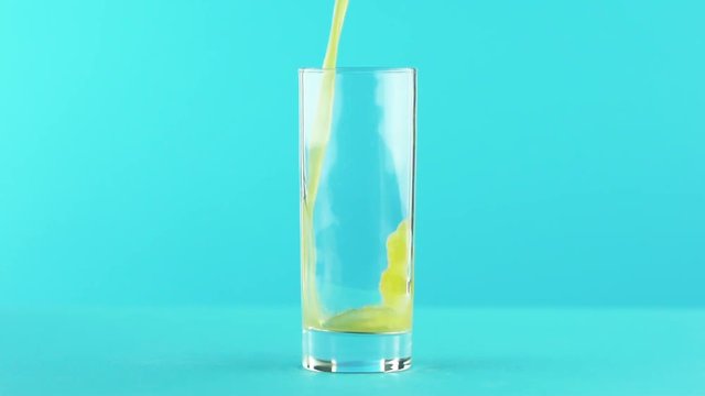Slow motion close-up shot of fruit orange multifruit juice cold beverage drink pooring into glass blue background in studio