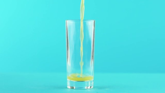 Slow motion close-up shot of fruit orange multifruit juice cold beverage drink pooring into low glass blue background in studio