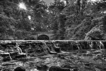 A black & white capture of a waterfall with a stone bridge in the background located in Cincinnati, OH.