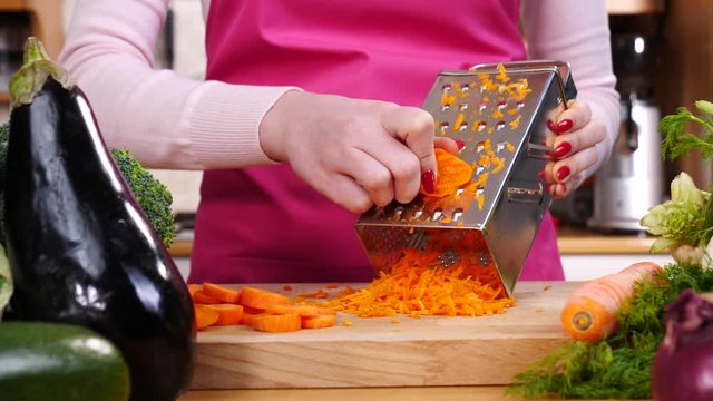 Close up of woman hand grating carrot on kitchen board in slow motion using vegetable grater.