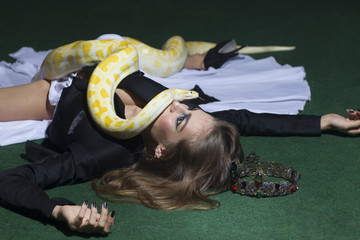 Fototapeta premium Python crawl on woman with long hair. Sensual woman with snake. Woman with makeup face and serpent. Beauty model in jewelry crown. Danger and fear concept