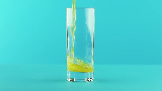 Slow motion close-up shot of fruit fizzy orange soda cold beverage drink pooring into low glass blue background in studio