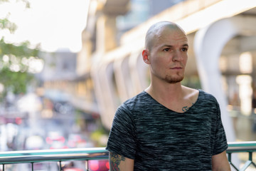 Young handsome bald man thinking on the foot bridge against view