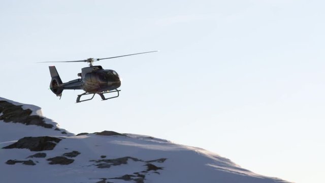 Black helicopter approaching for landing on snowy mountain