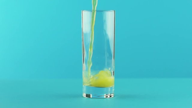 Slow motion close-up shot of fruit fizzy orange soda cold beverage drink pooring into glass blue background in studio