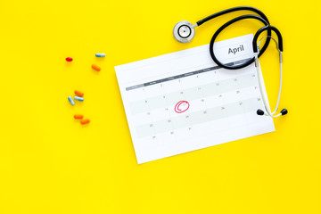 Planning medical examination concept. Regular medical examinations. Calendar with date circled, pills and stethoscope on yellow background top view copy space