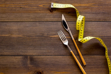 Proper nutrition for slimming. Fork, knife and measuring tape on dark wooden background top view copy space