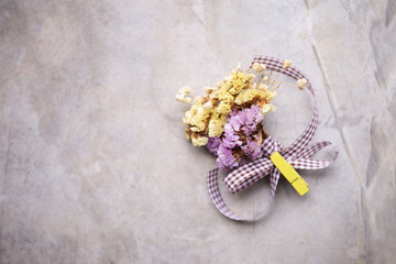 Boutonniere of dry mixed purple and yellow flowers with purple ribbon and yellow wooden clip with space on grey cement background, wedding day