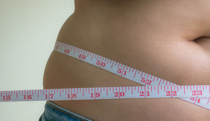 Close up of female hands measuring waist with measuring tape, dieting concept.