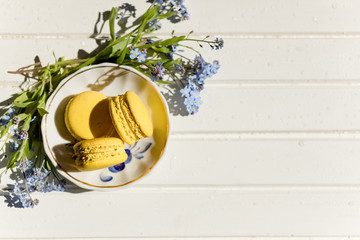 delicious colorful macaroons on trendy vintage wooden table with forget-me-not flowers and confetti, flat lay. tasty yellow, lemon macaroons. space for text. candy for party. Toned image