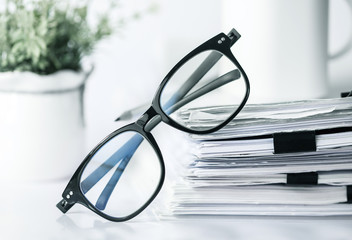 Close up black reading eyeglasses on stacking of office paper , business working document and information data concept. - obrazy, fototapety, plakaty