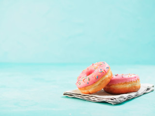 Two pink donuts on blue concrete background with copy space. Colorful donuts with copyspace. Glazed doughnuts with sprinkles