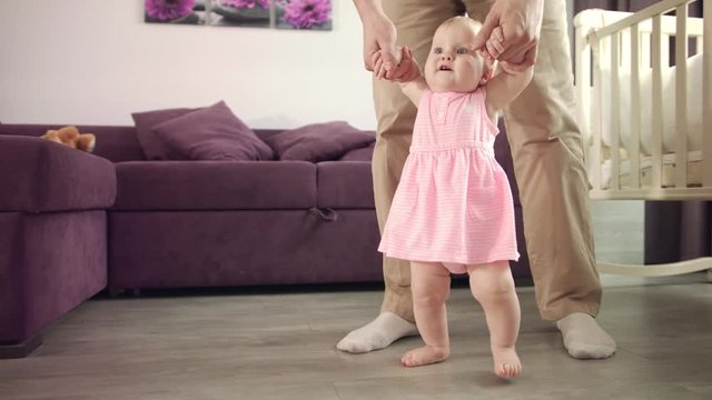 Baby learning walk. Father support daughter with first walk. Little kid trying make first step on floor at home. Child learning to walk. Dad holding kid and teach steping