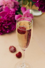 Glass of sparkling wine with cherry, summer drink, pink peony flowers on table