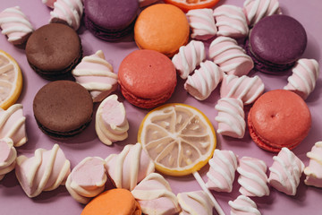 Flat lay of delicious sweet marshmallows and colorful macaroons on lilac background