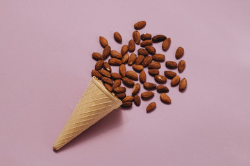 Crispy waffle cone with scattered almonds on purple background, food flat lay