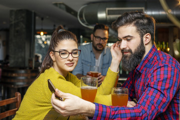 Young couple looking at mobile phone while sitting in local pub and drinking beer