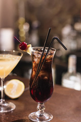 Delicious cocktail with ice cubes, cherry and straws in bar