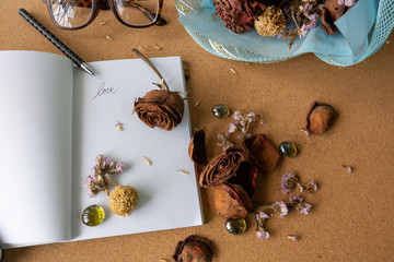 withered dry rose on white paper book with dried flowers and vintage sunglasses on cork background, old, memory, love concept
