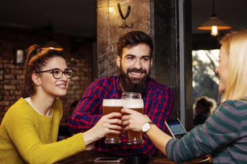 Group of four people toasting with glasses full of beer in local pub