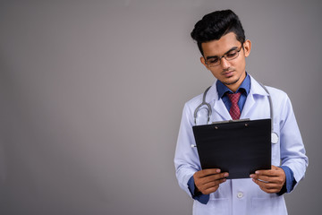 Young Indian man doctor against gray background