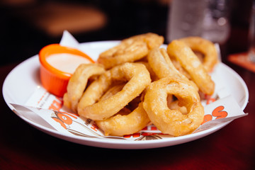 Onion rings served with sauce on white plate in the bar.