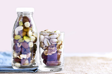 Dried fruits mix and variety of nuts in a bottle and glass on the brown sackcloth.