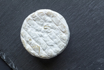 Whole round camembert cheese isolated on black slate board - top view