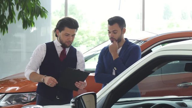 Young male customer talking to the salesman at the car dealership. Professional automobile dealer helping his client choosing new auto to buy. Profession, job, sales, transportation concept.