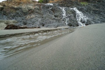 Natural waterfall over cliffs to sand beach.