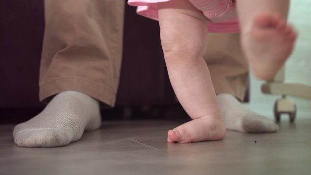 Infant feet learning walk. Close up of baby first step with father support. Daddy learning walk little baby. Little steps at home. Parent support concept. Baby feet walking on floor