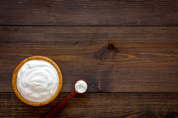 Obraz na płótnie Canvas Healthy product, healthy meal. Greek yogurt in brown bowl near spoon on dark wooden background top view copy space