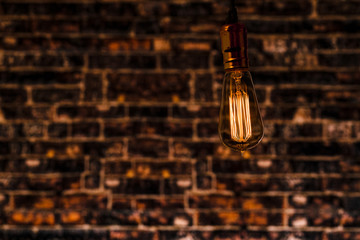 Edison Bulb in an Industrial Setting .An illuminated Edison Light Bulb in an industrial setting backed by an aged brick wall in low lighting