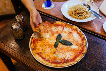 Hand taking slice of Margarita pizza topping with basil leaves served with oregano and chili powder.