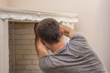 a man finishes decorating an artificial fireplace pasting the last gypsum stones to his walls