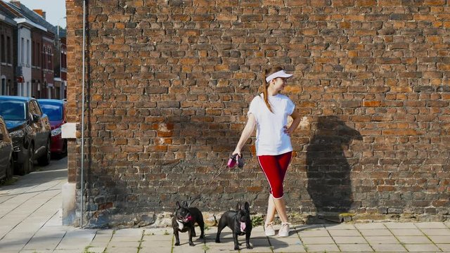 CINEMAGRAPH - SEAMLESS LOOP. Portrait of young Caucasian girl holding 2 black french bulldogs against brick wall