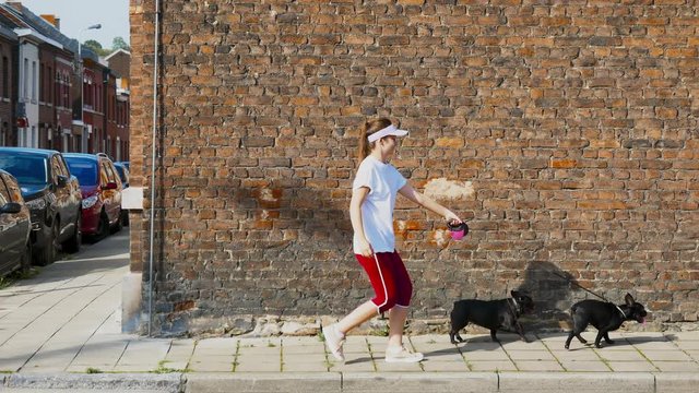 Portrait of young Caucasian girl taking walk with 2 black french bulldogs