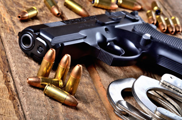 Obraz premium Pistol 9mm, bullets and handcuffs on old wooden table - view to the barrel