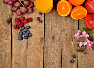 Fototapeta na wymiar Orange juice, fresh oranges, apples, grapes, raspberries, blueberries and spring flowers on a wooden table - view from above
