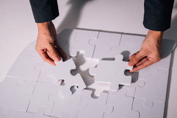 Hands of business man working on finishing last missing pieces of jigsaw on the white desk -...