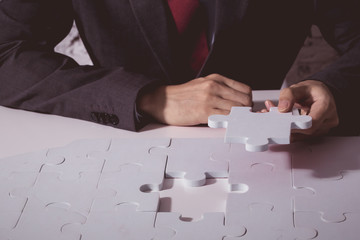 Young Businessman in suit holding the last missing piece of jigsaw and putting it to finish the critical thinking solution.