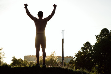 silhouette of a man at sunset, hands raised, victory, joy