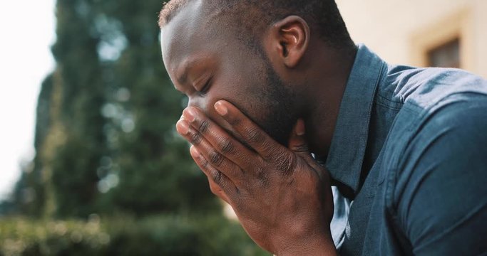 Sad and depressed young black african businessman sits tired after the call on the street. Concept of bad news, disappointment, illness