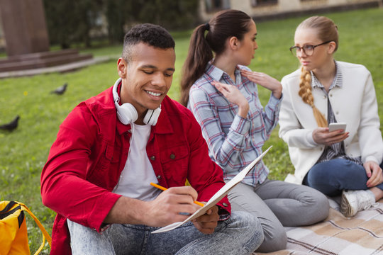 Fashionable student. Fashionable student wearing red jacket feeling happy while sitting near girls in the park