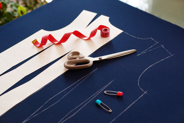 The process of sewing clothes from blue fabric. Paper pattern of the base of the dress on the fabric. Tailoring scissors and centimeter tape are items for sewing.